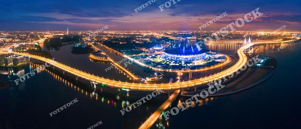 Панорамная фотография Санкт-Петербурга с высоты птичьего полета, на которой запечатлены улицы города, Крестовский остров, Финский залив и современный стадион. Вид с дрона позволяет увидеть масштаб городской инфраструктуры, широкие магистрали, водные пространства и архитектуру современного Петербурга. Снимок передает атмосферу динамичного мегаполиса, гармонично сочетающего природу и урбанистику. Фотография идеально подходит для туристических публикаций, фотостоков, рекламы, оформления интерьеров и материалов о современных достопримечательностях Санкт-Петербурга. Панорамный ракурс раскрывает красоту прибрежной зоны Финского залива и одного из самых известных спортивных объектов города.